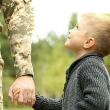 Young boy holds hands with soldier dad.