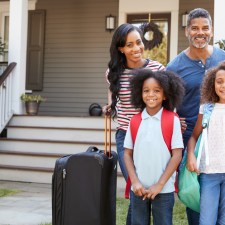 family with suitcases outside their home