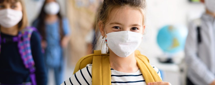 cute elementary school girl in classroom wearing mask