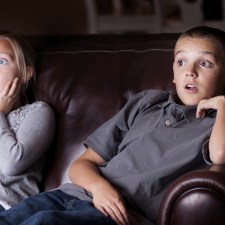 Boy and girl sitting on couch watching tv looking shocked