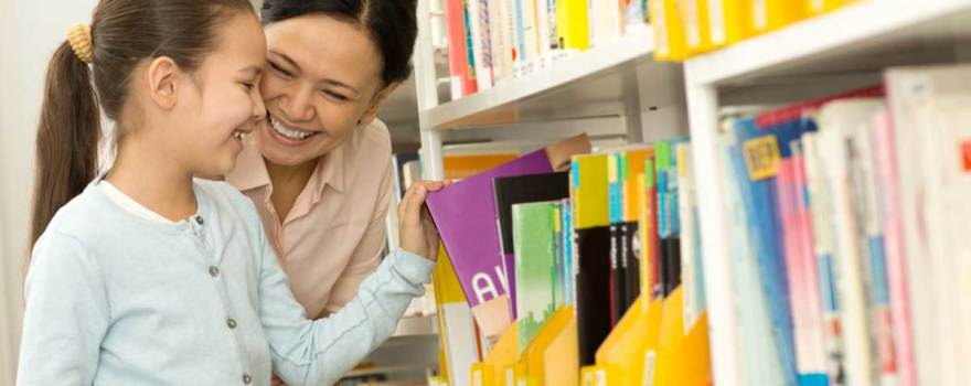 child and mother looking at books at public library