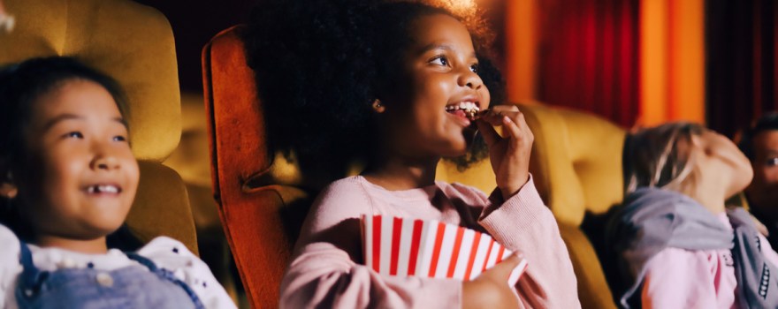 Kids eat popcorn and watch a movie at the movie theater