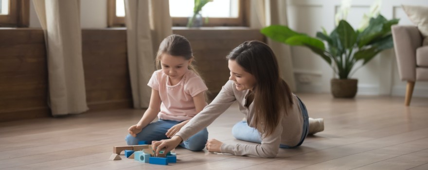 Happy mother and little daughter playing with toys together on wooden warm floor, smiling young mum and cute preschool girl having fun, spending time at home, underfloor heat, horizontal banner