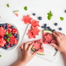 children's hands making salad on white table