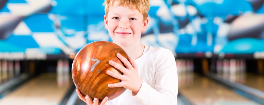 Child holding bowling ball at a bowling alley.