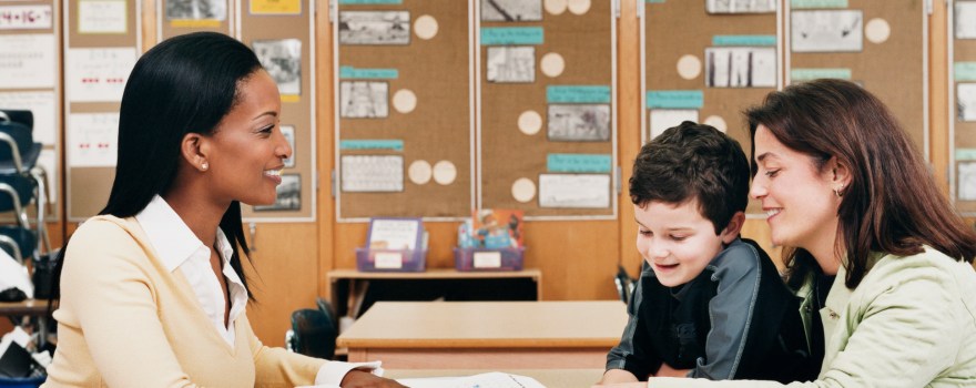 Two women and a little boy at a parent-teacher conference in a classroom.