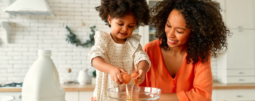 Parent and child preparing food together in a kitchen.