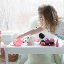 a little girl having a tea party with her doll, which shows one of many ways doll playing helps kids