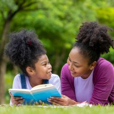 Mother and child on a lawn reading together. Reading is a way to fight summer learning loss.