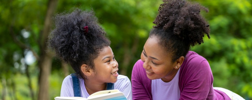 Mother and child on a lawn reading together. Reading is a way to fight summer learning loss.