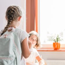 Four kids in a classroom near a window with sun coming through. One is standing and looks like she's starting a new school or class.