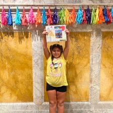 a little girl standing and holding up the story she wrote for a NYPL writing contest