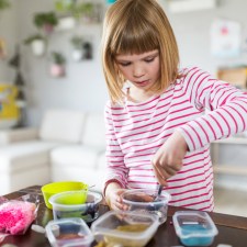 Little girl at home in her kitchen with bowls of different ingredients, showing how to make slime