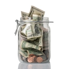 A jar for savings filled over the top with American coins and bills.