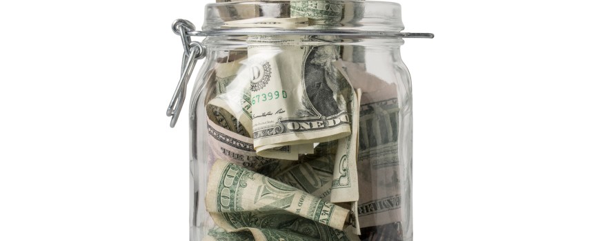 A jar for savings filled over the top with American coins and bills.