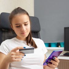 Teen girl at a desk social media spending with credit card and phone in hand